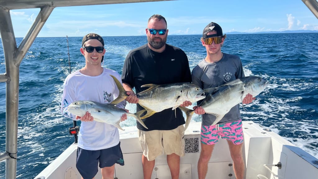 Three people proudly display their large catches aboard a boat, with the vast ocean stretching behind them. Enjoy the thrill of fishing in Playa del Coco or join a Costa Rica fishing charter for an unforgettable adventure on these vibrant waters.